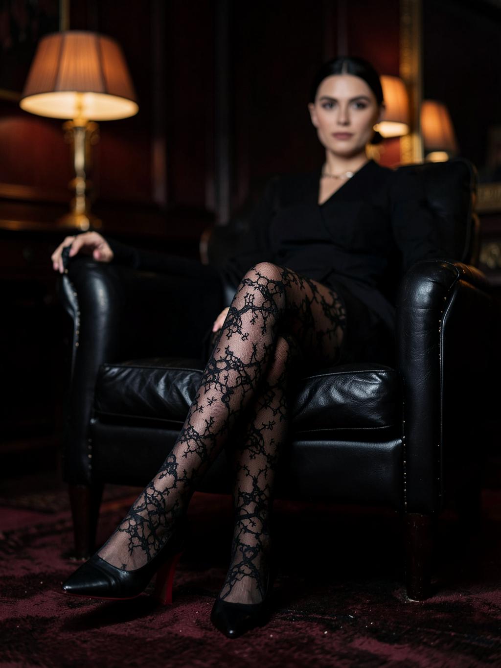 Gambe con calze nere velate su una poltrona in pelle scura, décolleté nere