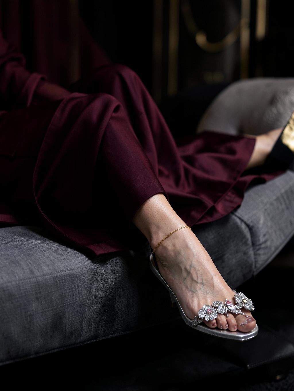 Sandali argento gioiello e sottile cavigliera dorata su una chaise longue grigia