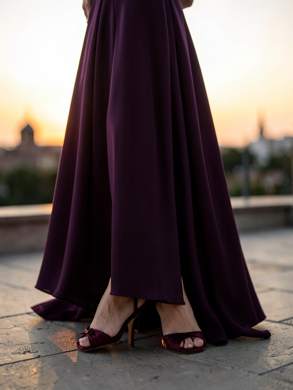 Abito lungo color prugna e sandali in raso bordeaux su una terrazza al tramonto